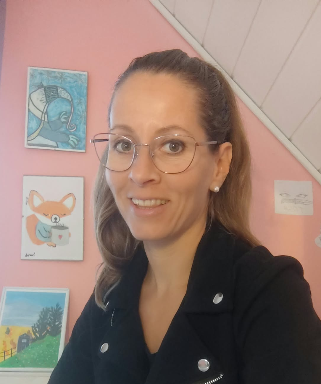 Virágmintás ruhás nő ül, oldalra néz, meleg színű fal előtt, háttérben képek és bútorok.